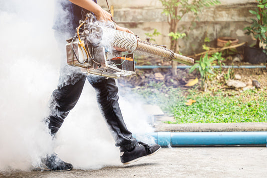 Man walking with a thermal fogger spraying chemicals in an outdoor environment creating a big cloud that follows behind him